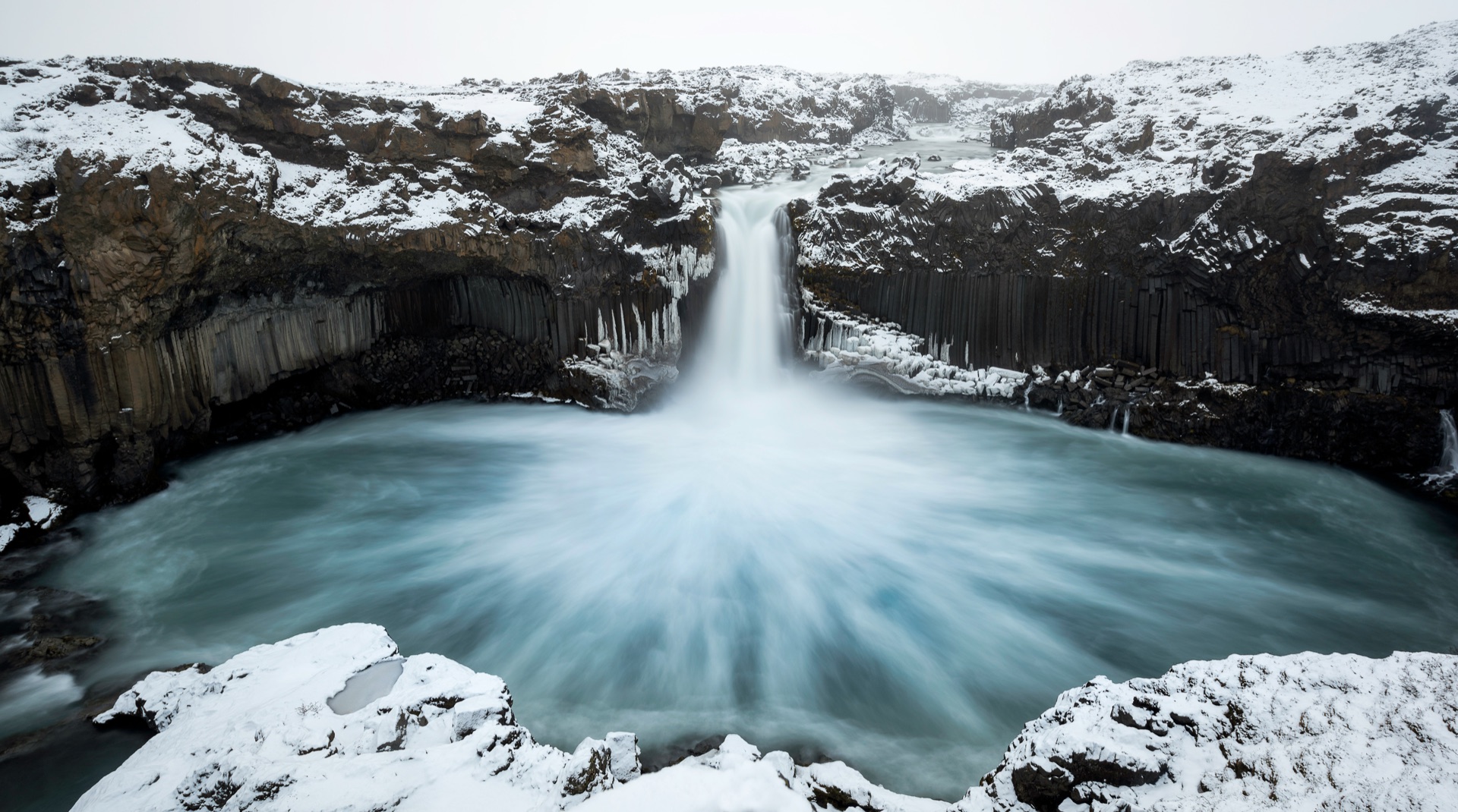 A waterfall flowing year-round between snow-covered basalt columns — a visual metaphor for an ongoing giving practice that lives across years